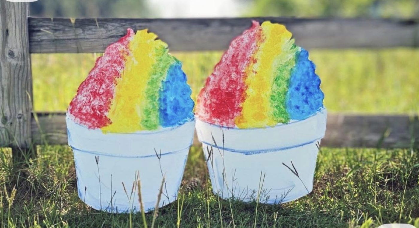 Two colorful rainbow shaved ice snowballs in cups on the grass